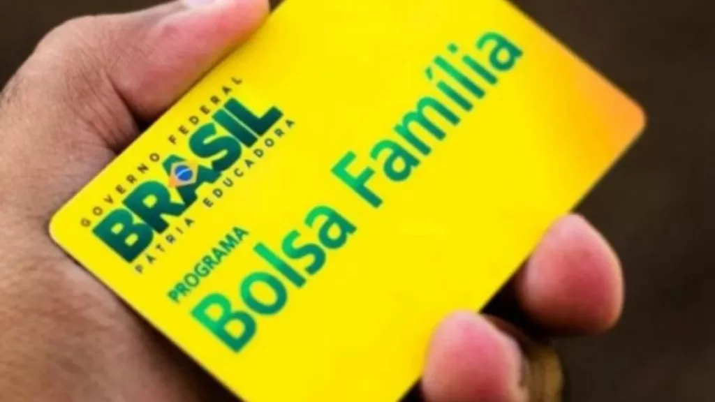 Cartão do Bolsa Família em primeiro plano com gráfico de queda e família que acaba de conseguir emprego formal ao fundo