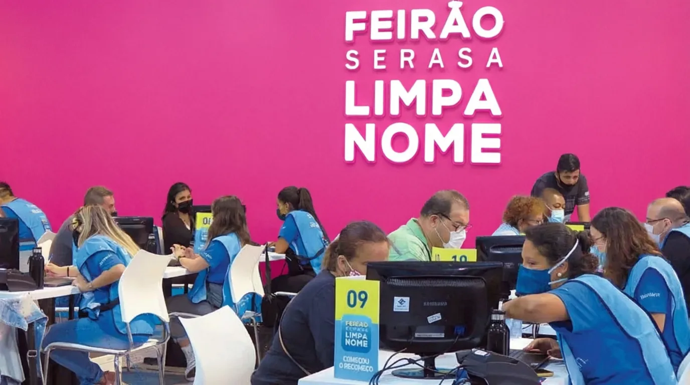 Evento Limpa Nome Serasa com atendentes em azul prestando atendimento ao público em frente a computadores com fundo rosa